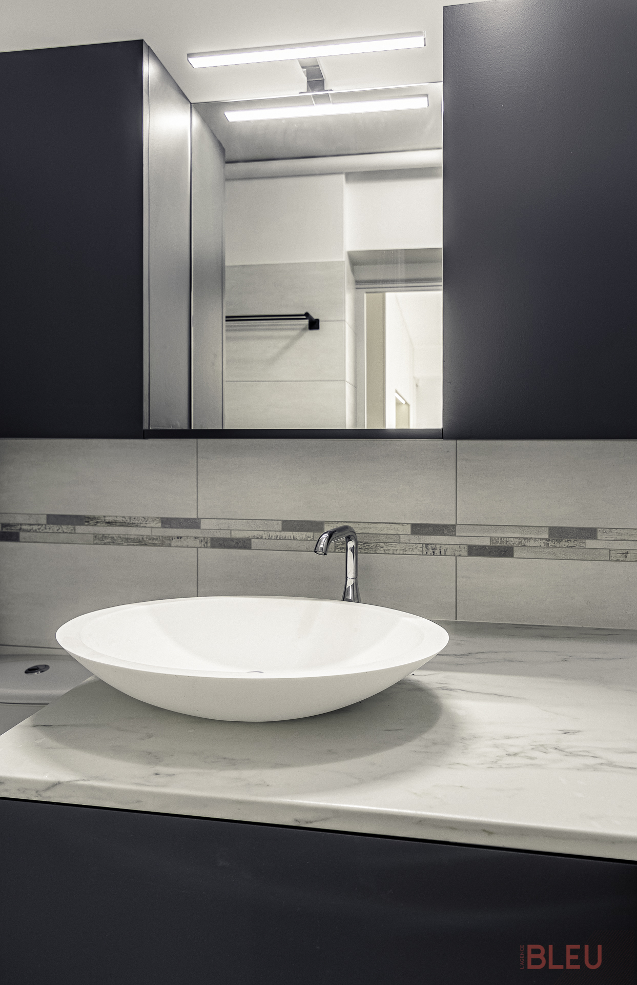 Cet agencement de salle de bain offre une utilisation optimale de l'espace. Le meuble vasque propose du rangement pour les articles de grande taille et un espace pour un lave-linge. Au-dessus, une tablette, un miroir, une applique et des meubles de rangement pour les objets plus petits. À gauche se trouve un cabinet de toilette traditionnel.