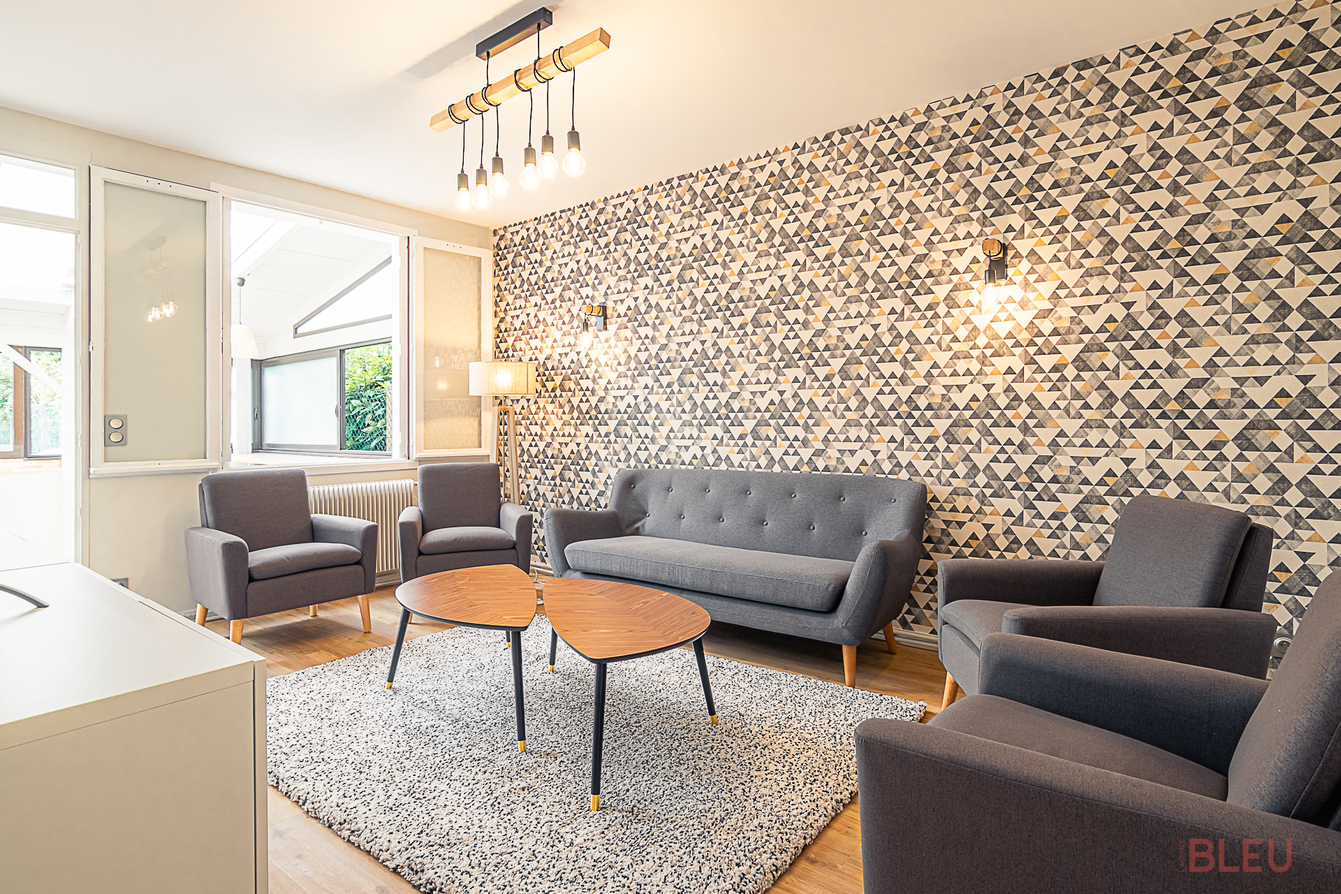 Salon moderne et lumineux avec mobilier gris, papier peint géométrique et éclairage industriel dans une maison de ville à Paris, conçu par un architecte d'intérieur.