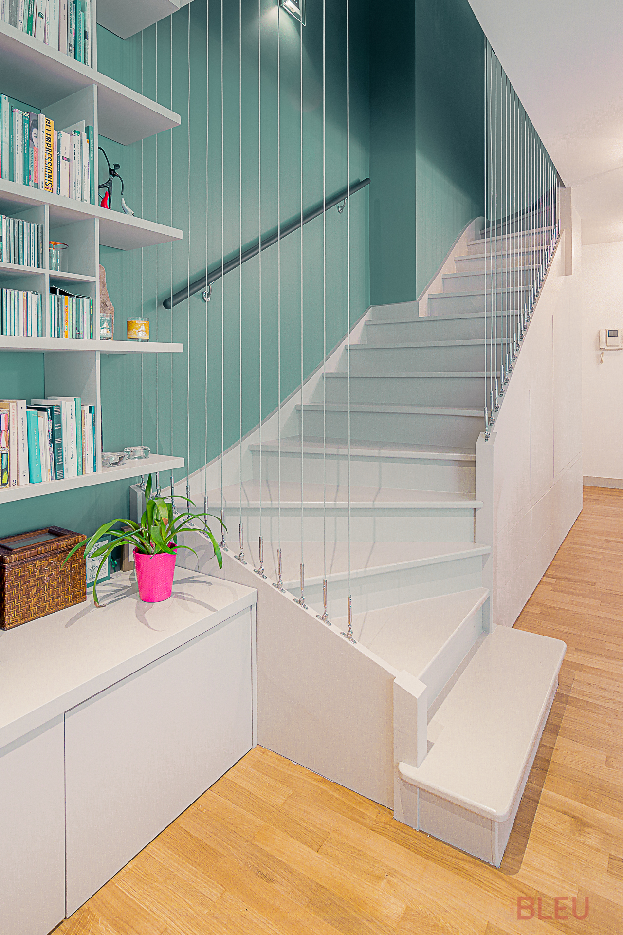 Espace de vie moderne avec escalier blanc, mur vert foncé, bibliothèque intégrée et parquet clair - Projet de rénovation d'appartement duplex à Paris par notre agence d'architecture intérieur
