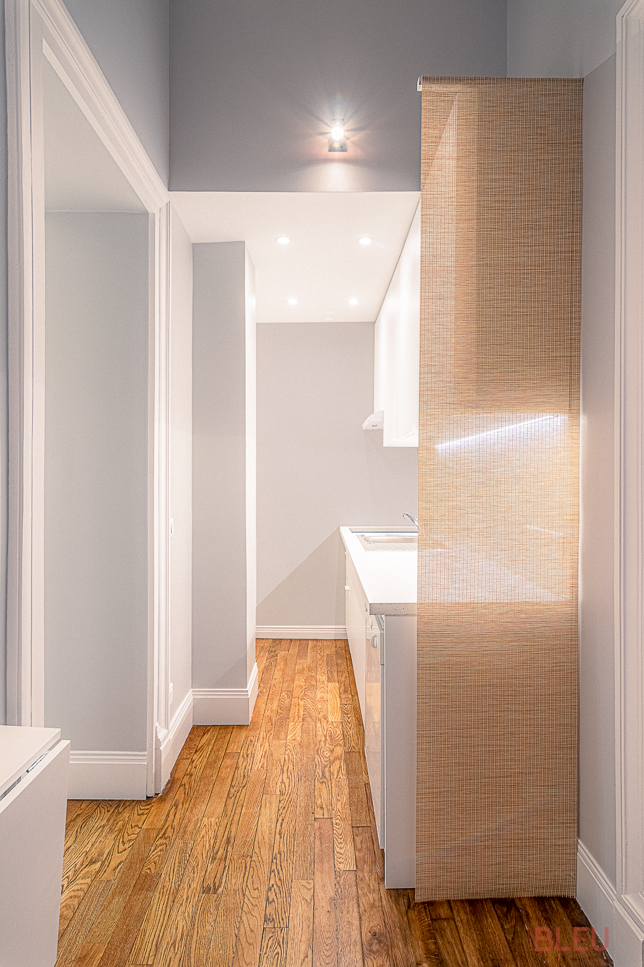 Petite cuisine moderne et minimaliste avec parquet clair, armoires blanches et cloison en bambou - Projet de rénovation appartement haussmannien à Paris par notre agence d'architecture intérieur